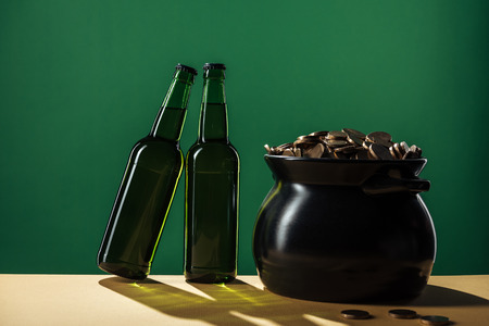 beer bottles and black pot with golden coins isolated on green, st patrick day concept