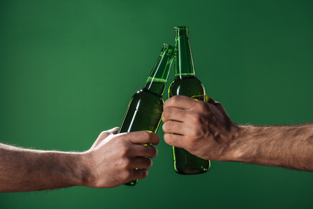cropped view of men clinking beer bottles isolated on green, st patrick day conceptの写真素材