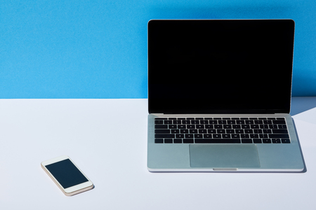 laptop with blank screen and smartphone on white desk and blue backgroundの写真素材