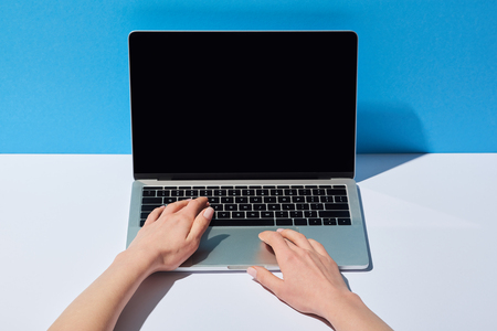 cropped view women using laptop with blank screen on white desk and blue backgroundの写真素材
