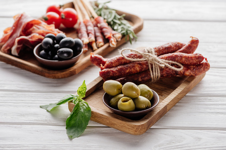 food composition with various meat appetizers, olives and basil leaves on white wooden surfaceの写真素材