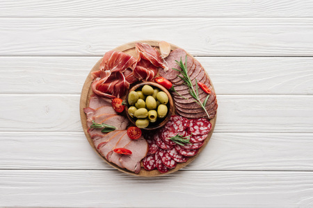 top view of arrangement of various meat snacks and olives on white wooden backdropの写真素材