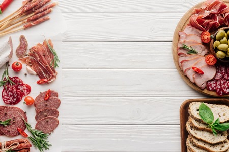 top view of arrangement of various meat snacks and olives on white wooden backdropの写真素材