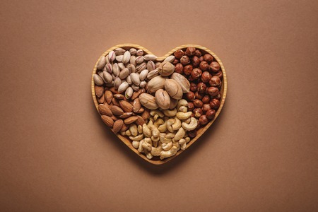 top view of assortment of various nuts in heart shaped box on brown backdropの写真素材