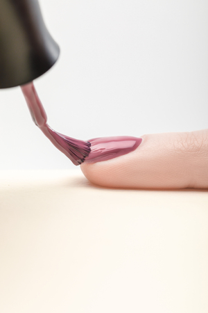 shiny purple nail polish on fingernail of woman on grey backgroundの写真素材