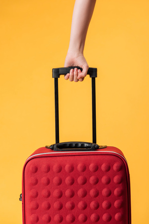 cropped view of woman holding red travel bag isolated on yellowの写真素材