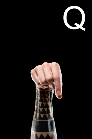cropped view of tattooed hand showing latin letter - Q, deaf and dumb language, isolated on blackの写真素材