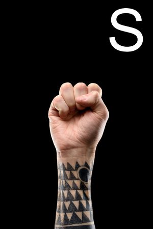 cropped view of tattooed hand showing latin letter - S, deaf and dumb language, isolated on blackの写真素材