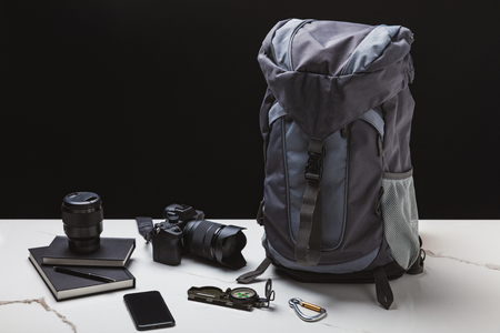 backpack, smartphone, compass, notebooks and photo camera with lens on blackの写真素材