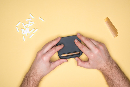 Cropped view of young man making cigarettes isolated on yellowの写真素材
