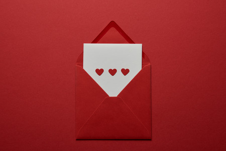 top view of white letter with hearts in envelope on red background