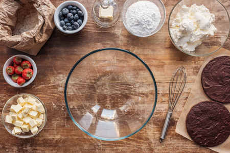 Top view of empty glass bowl, whisk and ingredients for delicious homemade cake on wooden tableの写真素材