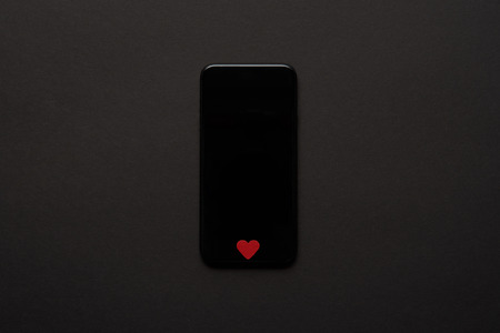 top view of smartphone with blank screen and small red heart sign on dark backgroundの写真素材