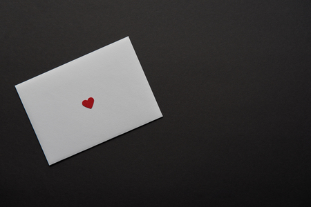 top view of white greeting card with red heart sign isolated on black