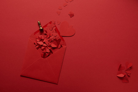 top view of paper cut hearts and opened envelope on red backgroundの写真素材