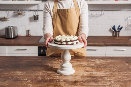 Cropped shot of woman in apron cooking delicious sweet cake with creamの写真素材
