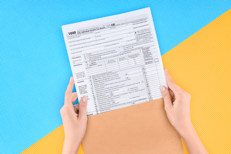 Cropped view of woman holding tax form on blue and yellow background