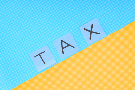 Top view of word 'tax' made of cards on blue and yellow backgroundの写真素材