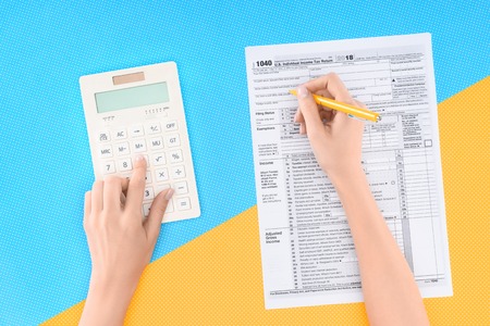 Cropped view of woman using calculator and filling tax form on blue and yellow background