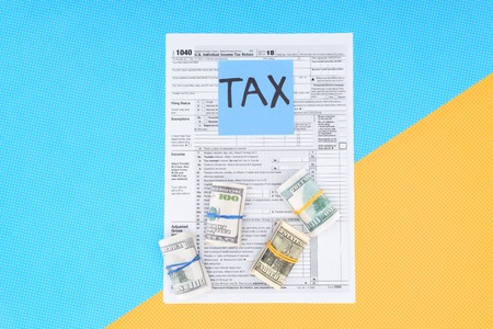 Top view of tax form, money rolls and card with 'tax' word on blue and yellow backgroundの写真素材