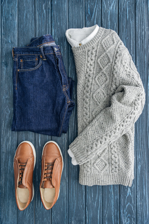 Flat lay of grey knitted sweater, jeans and shoes on wooden backgroundの写真素材
