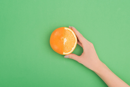 cropped view of female hand with fresh partially cut orange on green backgroundの写真素材