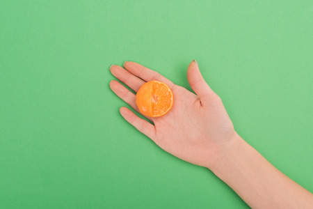 partial view of female hand with partially cut tangerine on green background