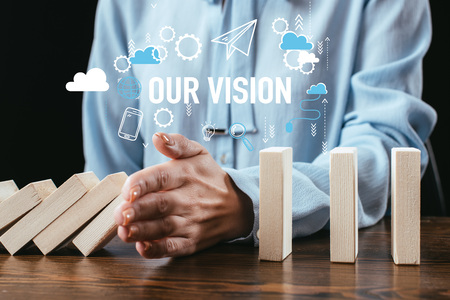 selective focus of woman preventing wooden blocks from falling with icons and 'our vision' words on foregroundの写真素材