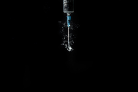syringe with smoke or paint swirls isolated on blackの写真素材
