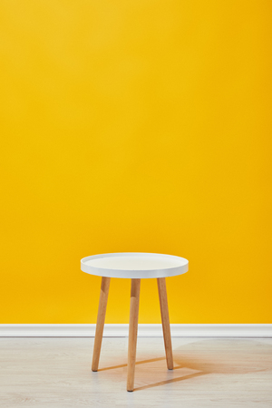 Minimalistic little wooden table near yellow wallの写真素材