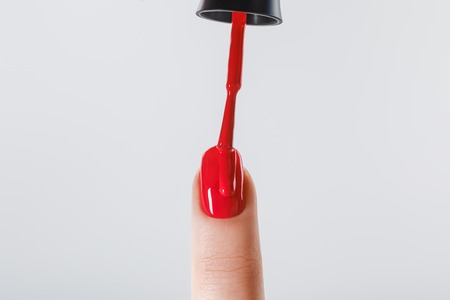 cropped view of woman applying red nail polish on fingernail isolated on greyの写真素材