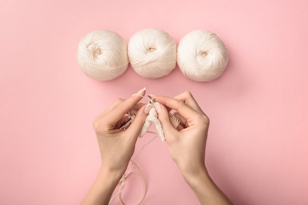 partial view of woman knitting yarn on pink backgroundの写真素材