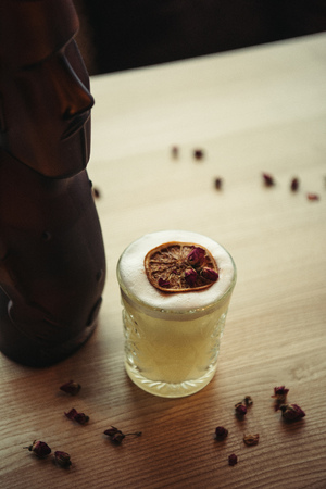 selective focus of bronze statue and alcoholic cocktail decorated with dry orange and flowers on wooden table in restaurantの写真素材