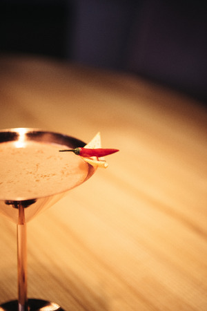 selective focus of alcoholic cocktail in metal glass decorated with chili pepper and nacho chip on wooden tableの写真素材