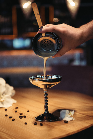 selective focus of bartender pouring cocktail from shaker through sieve in metal glassの写真素材