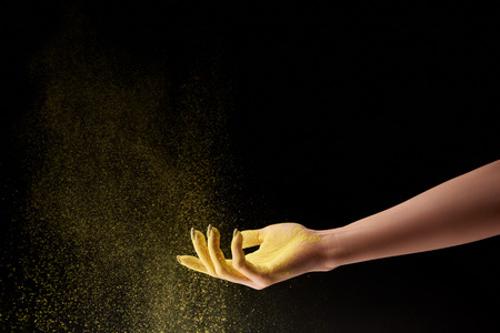 Cropped view of woman and yellow holi powder on black background