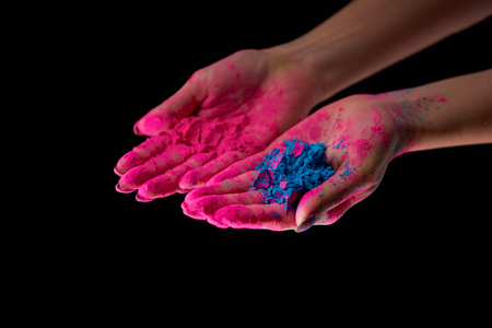 cropped view of adult with hands in pink powder holding blue holi powder isolated on blackの写真素材
