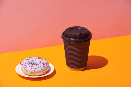 tasty donut with saucer and paper coffee cup on yellow surface and pink backgroundの写真素材