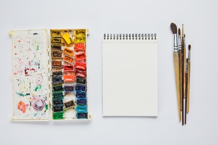 top view of album with watercolor paints and paintbrushes on white backgroundの写真素材
