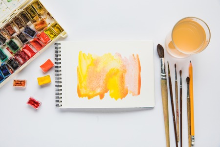 top view of album with watercolor paints, brushes and glass of water on white backgroundの写真素材
