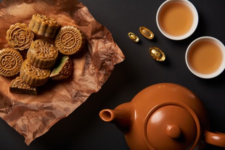 top view of mooncakes, tea pot and gold ingots isolated on blackの写真素材