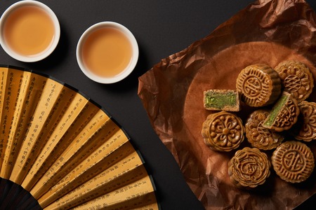 Top view of traditional chinese mooncakes with tea and hand fan isolated on blackの写真素材