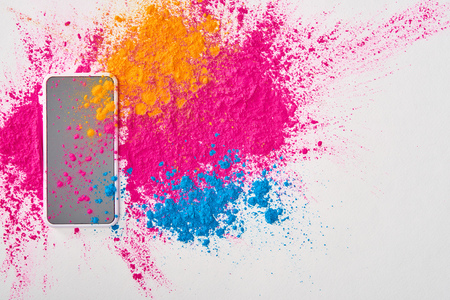 top view of smartphone and explosion of multicolored holi powder on white backgroundの写真素材