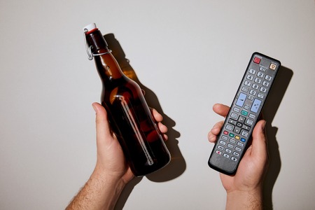 cropped view of man holding bottle with beer and remote control in hands on white backgroundの写真素材