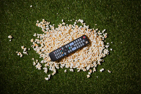top view of popcorn lying near remote control on green grassの写真素材