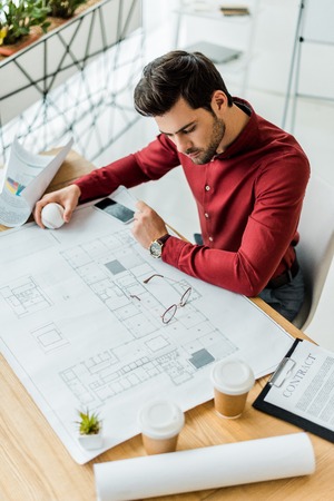 handsome male architect sitting and working on blueprint in officeの写真素材
