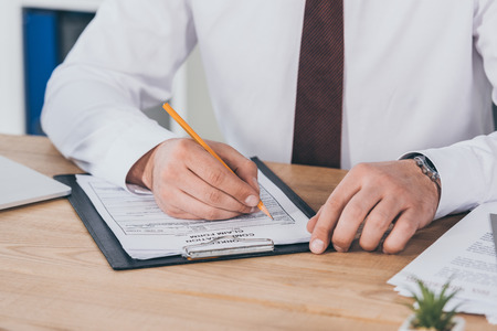 cropped view of businessman writing on compensation claim form at workplace