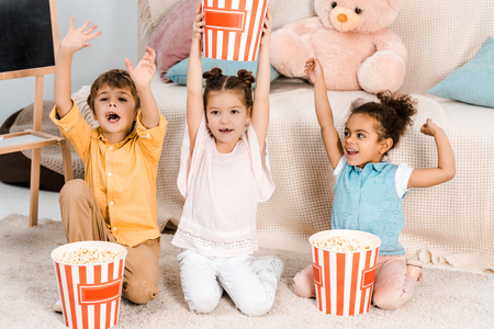 cute happy children sitting on carpet and holding boxes with popcornの写真素材