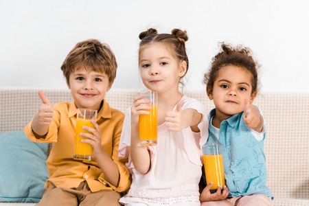 cute multiethnic kids holding glasses of juice and showing thumbs upの写真素材