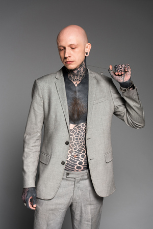 stylish tattooed man in grey suit holding chain and looking down isolated on greyの写真素材